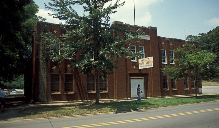Two-story brick building with trees and sign above its front door