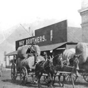 Men transporting cotton bales with horse-drawn wagons on town road