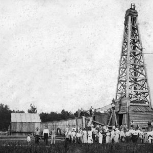 group of people pose in front of wooden oil derrick