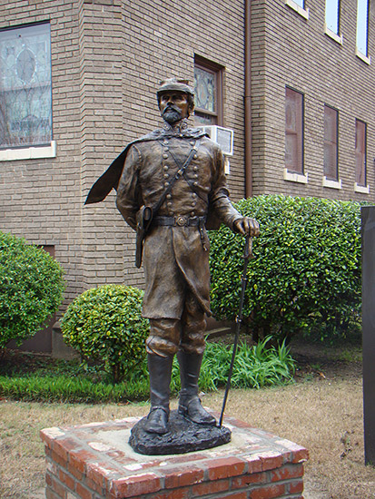 Bronze statue of white man in military uniform with sword in front of brick building