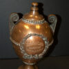 Copper urn with inscription and wreath detail on shelf