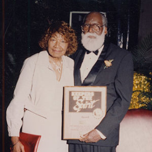 African-American man and woman holding award plaque and purse respectively