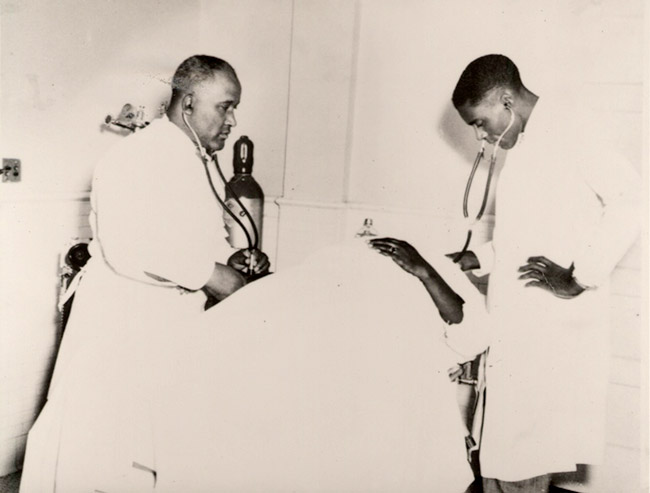 Two African-American male doctors examining a patient in bed