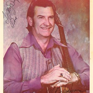 signed photo with white man in purple shirt and vest holding an acoustic guitar