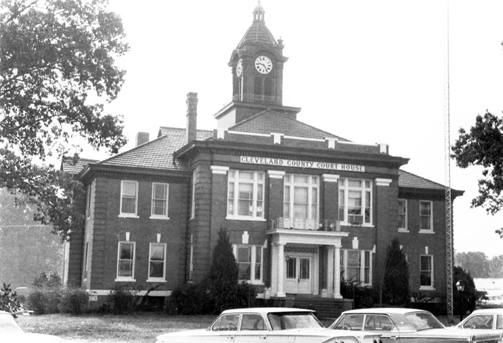 Multiple-story building with "Cleveland County Court House" written above the entrance and below its clock tower