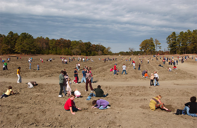 Crowd of tourists digging in dirt field for diamonds
