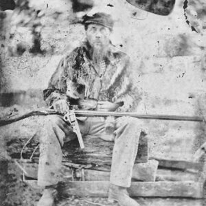 White man sitting with pistol in hand and rifle across his lap