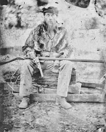 White man sitting with pistol in hand and rifle across his lap