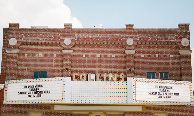 Brick theater building with white "Collins" marquee covered in multicolored lights