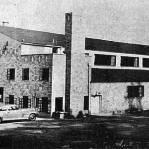 Brick auditorium building with "Colony House" sign and cars parked in front