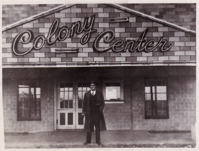Man standing before building with sign "Colony Center"