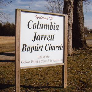 "Welcome to Columbia Jarrett Baptist Church" sign with trees and gravel road behind it