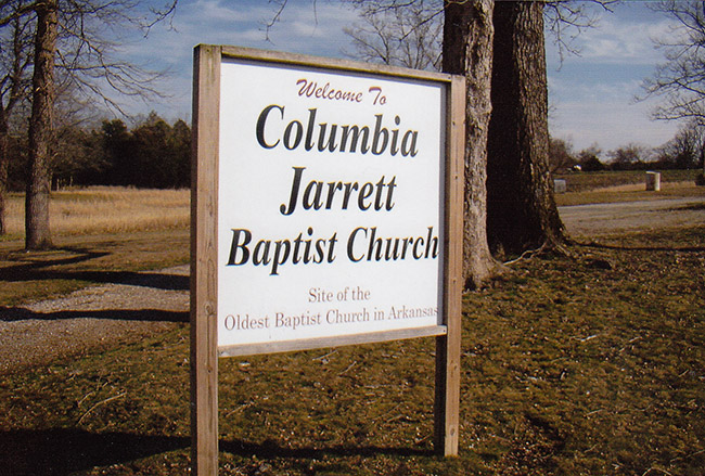 "Welcome to Columbia Jarrett Baptist Church" sign with trees and gravel road behind it