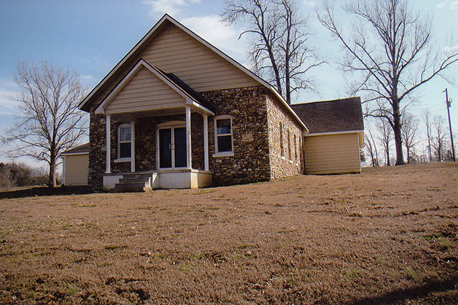 Single-story house with covered porch and stone walls on hill
