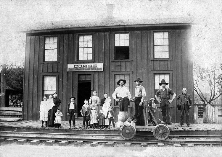 White adults and children pose with handcar outside wood frame "combs" train station