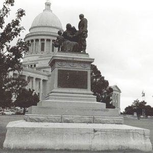 Front view of stone monument with statues atop pedestal with Capitol building behind it
