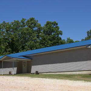 Single-story building with siding covered entrances and blue roof on gravel road