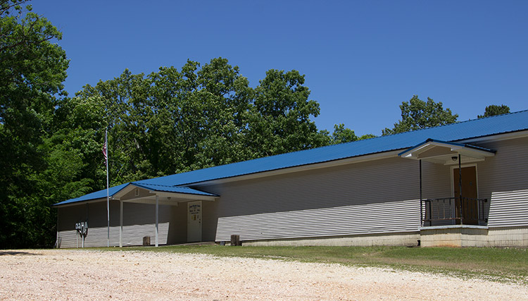 Single-story building with siding covered entrances and blue roof on gravel road