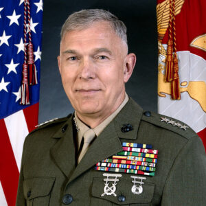 White man in military uniform featuring medals with flags beside him