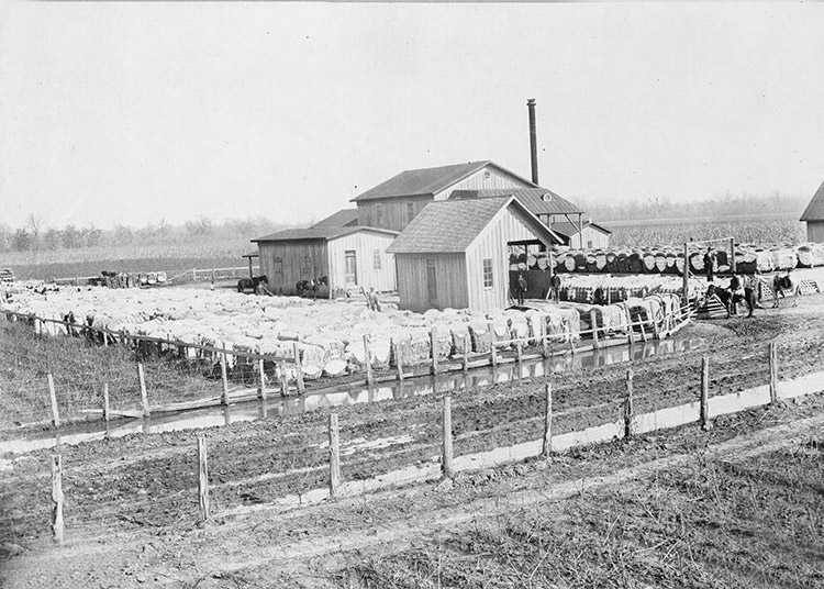 Mill buildings with bales of cotton inside fence