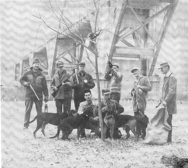 group of white men with hunting dogs beneath bridge