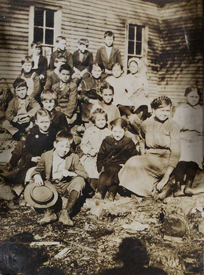 Group of white children and white woman outside school house