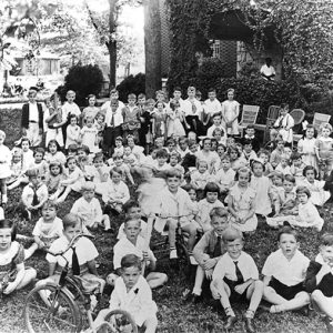 Group of white children sitting on grass outside brick house