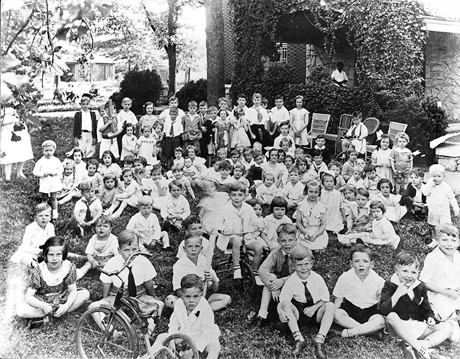 Group of white children sitting on grass outside brick house
