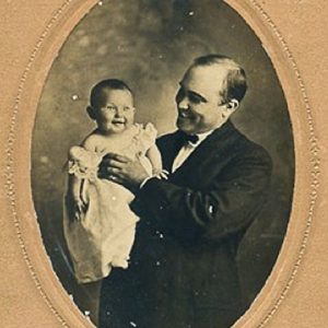 White man in suit and bow tie holding his baby