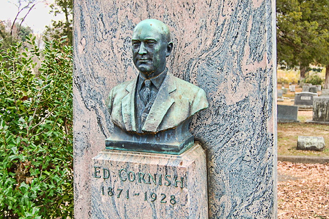 Green oxidized bust of Ed Cornish on pedestal with graveyard in backgroun