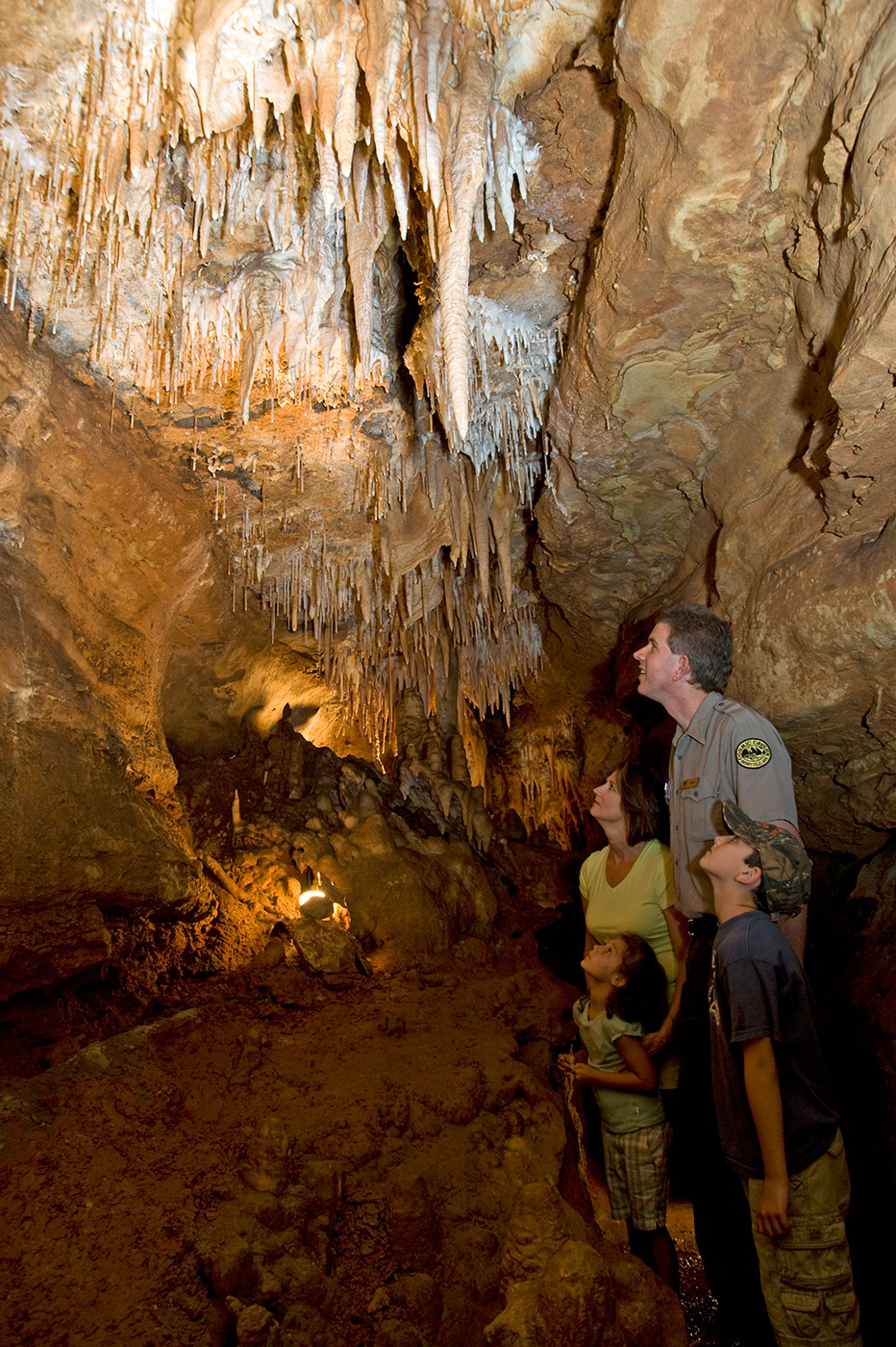 White park ranger and white woman and children marveling inside a deep cave with stalactites hanging from above