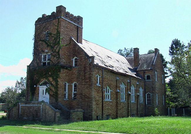 Multistory brick building with ivy on the side and arched windows and tower on grass