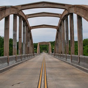 Two-lane road across concrete arch bridge with railings