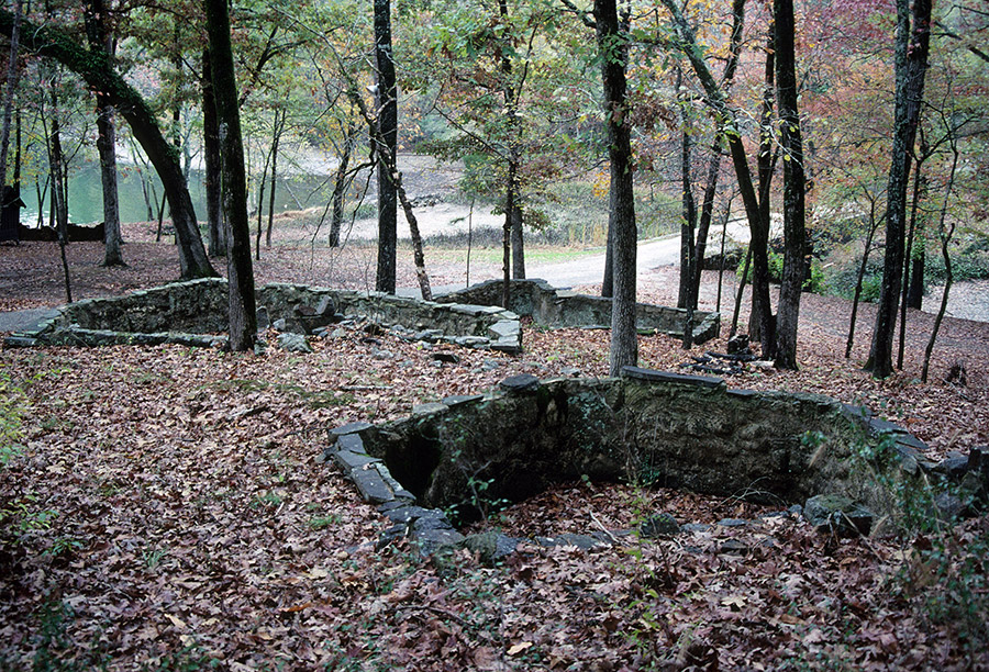 Pits with stone walls in woods next to road near a pond