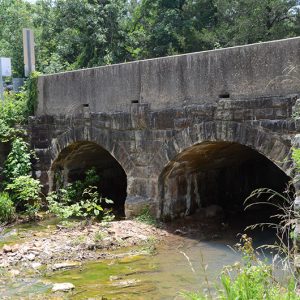 Side view of concrete and stone arch bridge over creek