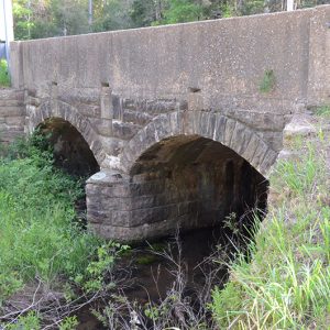 Side view of concrete and stone arch bridge over creek
