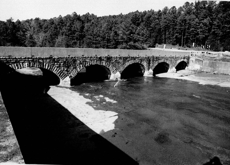 Brick arch spillway bridge with concrete platform and trees in the background