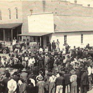 Large group of people milling about on the downtown square with storefronts