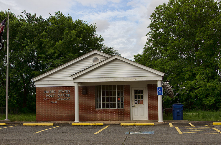 Single-story brick building with covered entrance on parking lot with flag pole