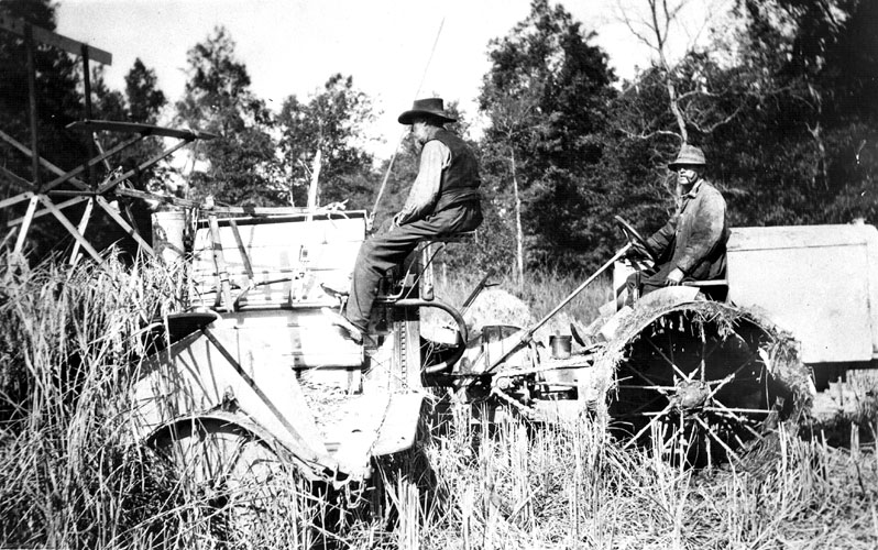 White farmer in cowboy hat and vest driving a harvester