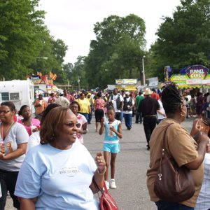 Crowd of African-American men women and children at festival with souvenir shops and food stands in the background