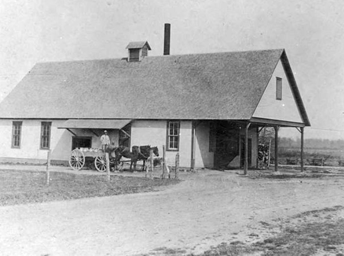 Man and horse-drawn wagon outside single-story building with covered entrance