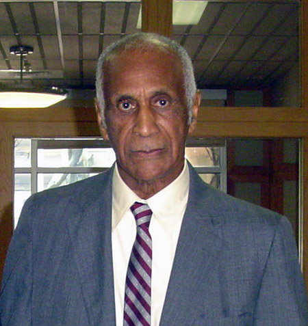 older black man with serious expression and short white hair and sideburns in suit jacket and striped tie