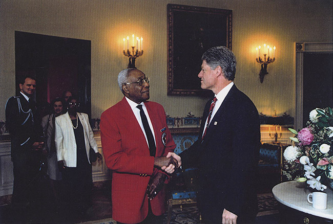 Older African American man in red jacket shaking hands with white man in suit in formal room