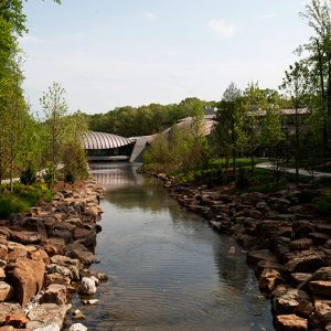 Creek with rock shores lined with trees and modern building in the background
