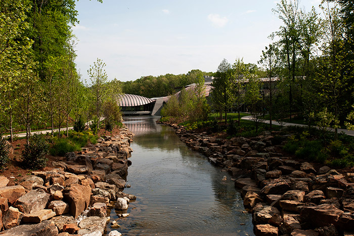 Creek with rock shores lined with trees and modern building in the background