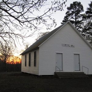 Single-story white church building with two front doors with trees and sunset behind
