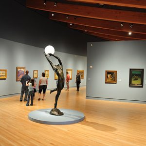 Statue of woman dancing with ball light in museum gallery with visitors