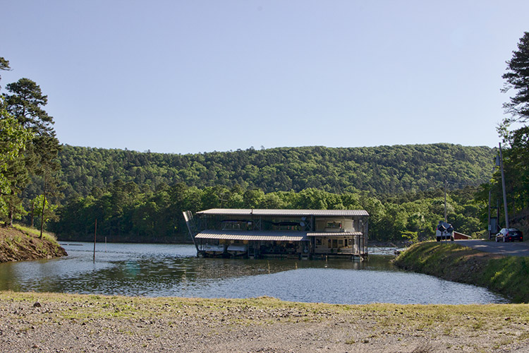 Multistory marina floating in lake next to shore road with tree covered hills in the background