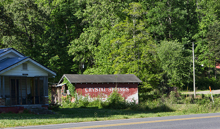 Single-story house and red barn with "Crystal Springs" written on its side next to two-lane highway